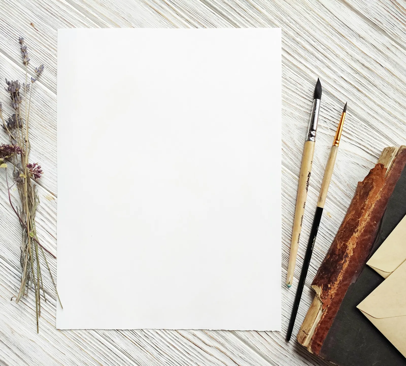 Hoja de papel en blanco con pinceles sobre una mesa clara
